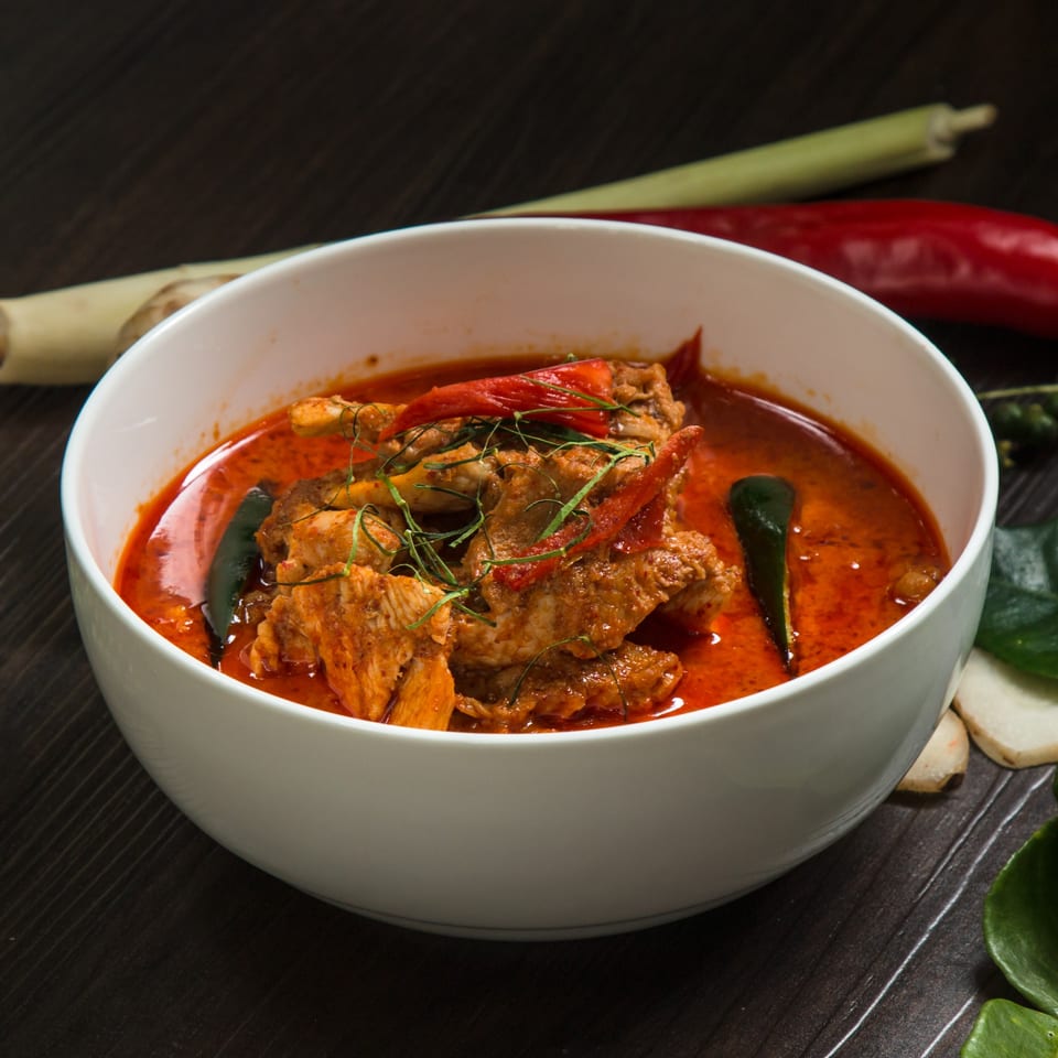 Tuk Tuk Express's red curry with chicken, chili, and herbs in a white bowl.