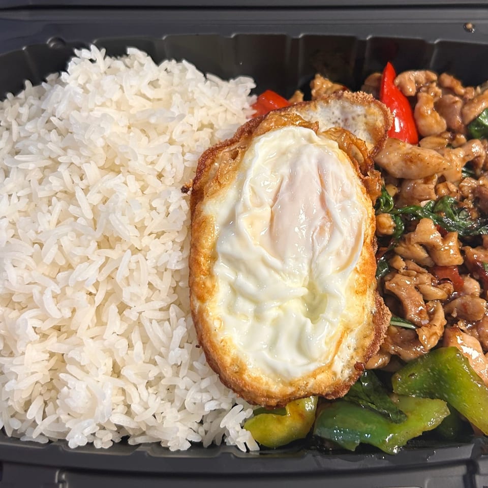 Tuk Tuk Express's Thai basil chicken with white rice and a fried egg in a black takeout container.