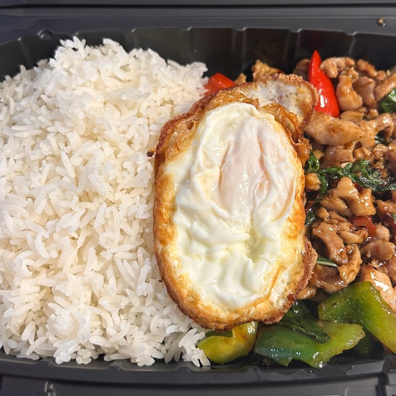 Tuk Tuk Express's Thai basil chicken with white rice and a fried egg in a black takeout container.