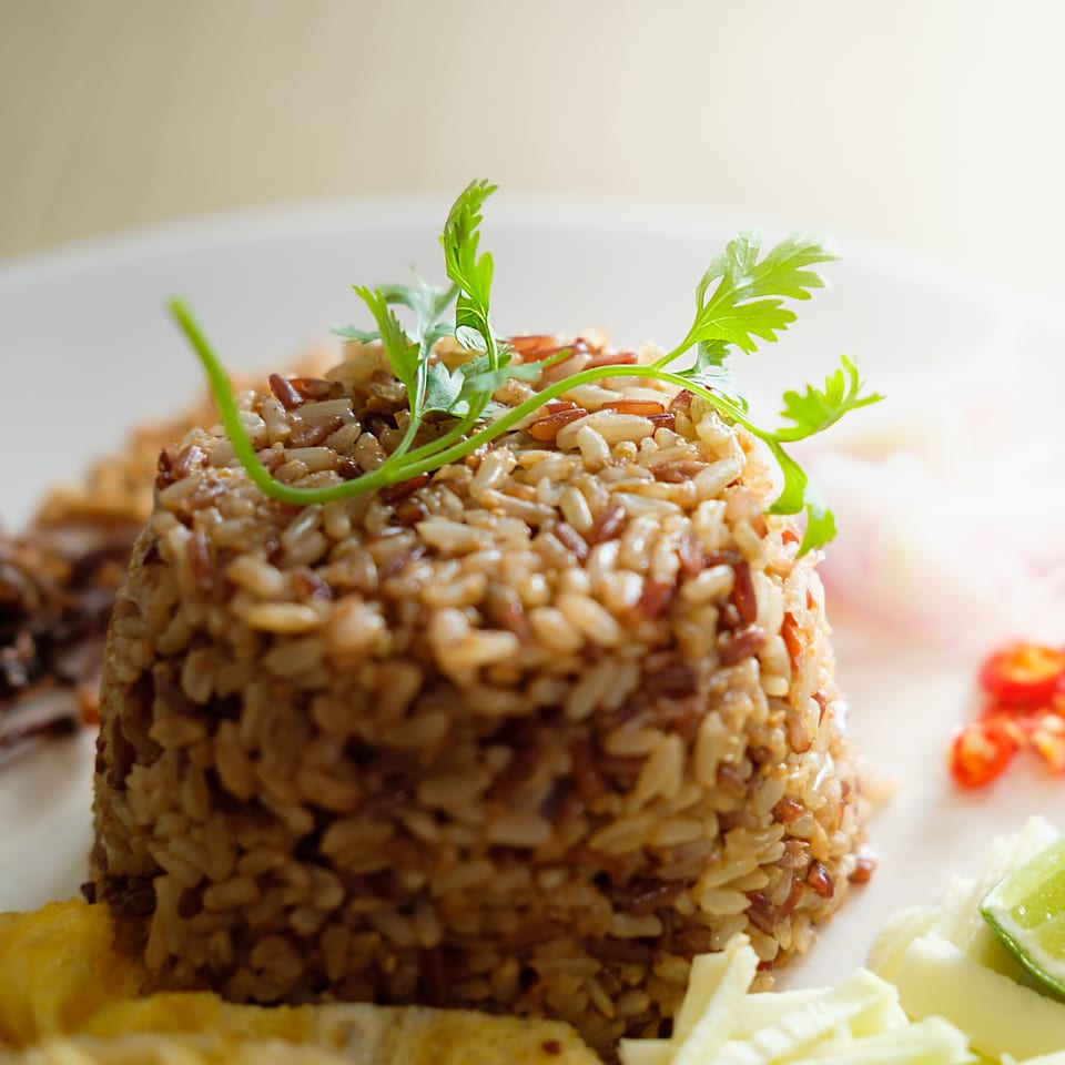 Close-up of Thai fried rice with herbs, chili, and lime on a white plate.