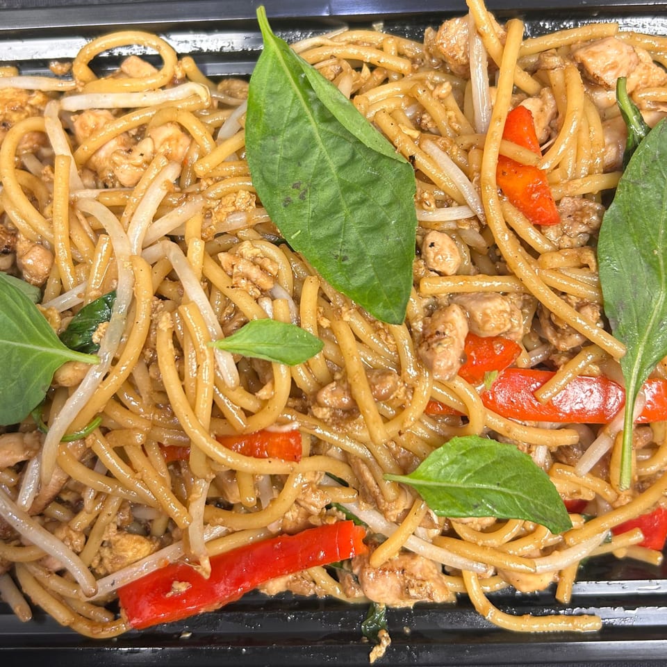 Close-up of Thai drunken noodles with chicken, red bell peppers, bean sprouts, and basil.