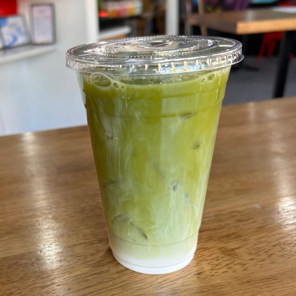 Iced green tea latte with milk and ice in a clear plastic cup on a wooden table.