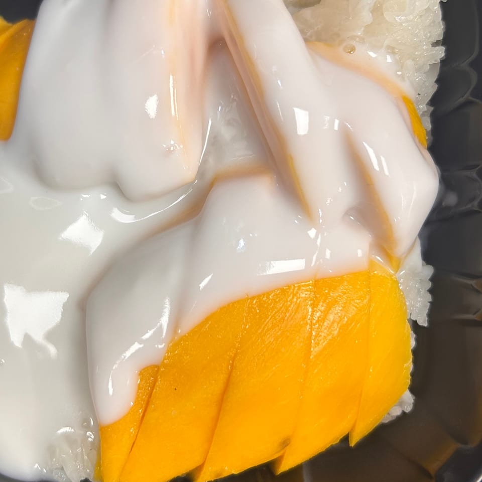 Close-up of mango sticky rice with white coconut cream drizzled over bright yellow mango slices.