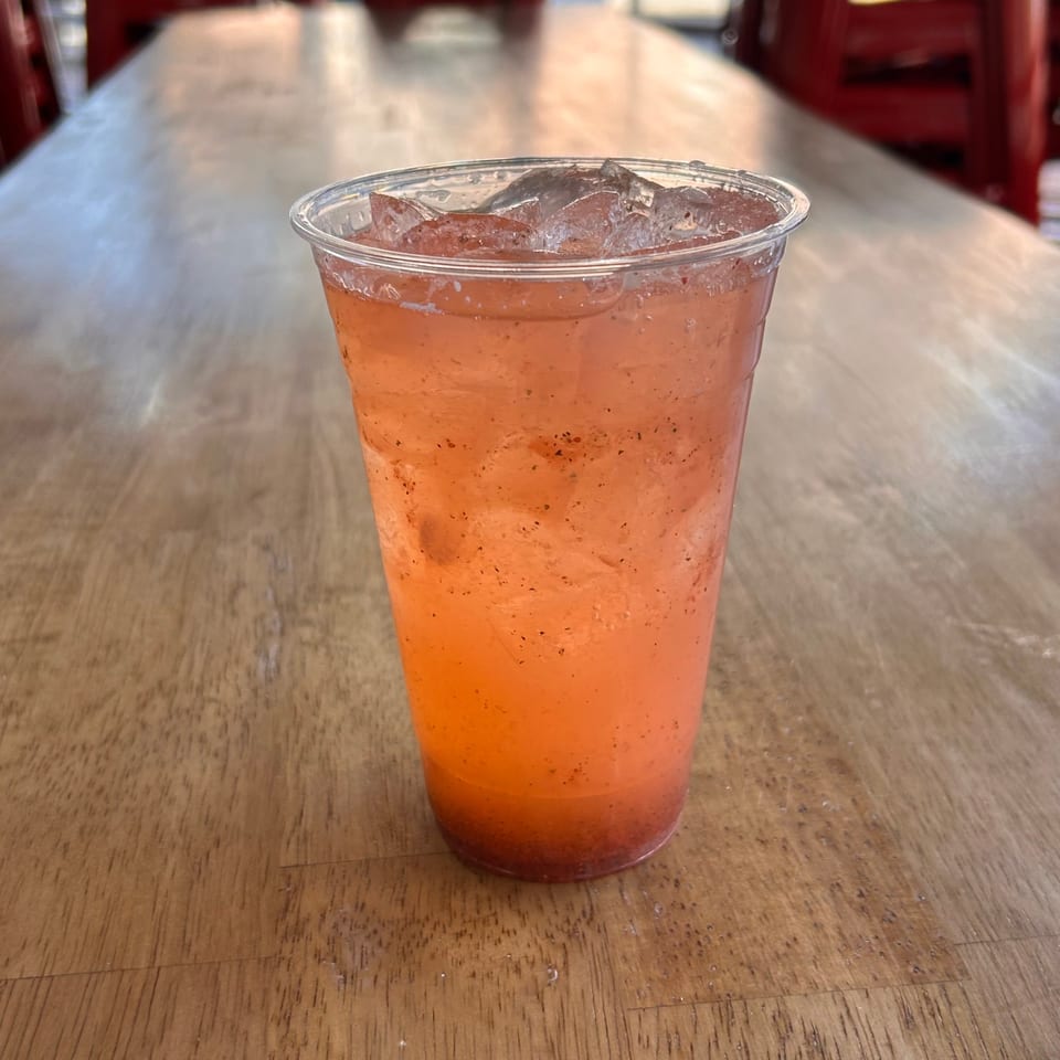 A refreshing iced strawberry drink with seeds, in a clear plastic cup on a wooden table.